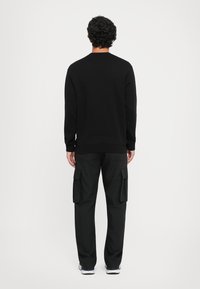 Sweatshirt preto e calças de carga pretas. O sweatshirt tem um decote redondo e mangas compridas. As calças de carga apresentam bolsos laterais e um corte largo.