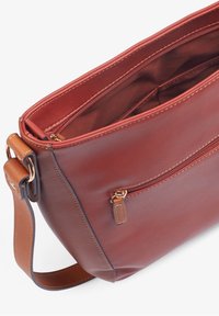 Bolso de hombro de cuero marrón con una textura suave, que cuenta con un compartimento principal con cremallera y un bolsillo exterior, complementado por una correa en color marrón claro.
