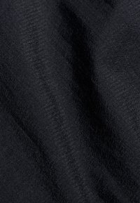 Gros plan sur un tissu noir texturé avec des motifs diagonaux subtils et des ombres douces mettant en valeur sa surface tissée.