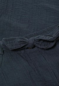 Tumši zilas krāsas audums ar teksturētu izskatu, ar svārku daļu viduklī un elastīgu jostasvietu; redzamākā sarežģīta diegu šuvēšana.