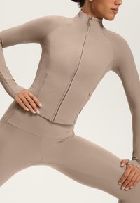 Langärmlige Sportjacke in hellem Beige, aus geripptem und glattem Material, mit durchgehendem Reißverschluss und figurnaher Silhouette.