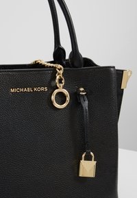 Borsa a tracolla in pelle nera con superficie testurizzata, hardware dorato, dettaglio a catena e ciondolo a forma di lucchetto. Presenta manici doppi e logo del brand.