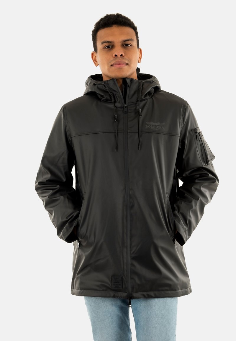 Giubbotto impermeabile nero con cappuccio, chiusura frontale con zip e dettagli a pressione. Presenta una tasca con zip sulla manica e una texture liscia e lucida.