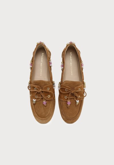 Mocassins en daim marron avec nœuds papillon et perles roses, blanches et dorées le long des bords et des lacets, étiquetés Stuart Weitzman à l'intérieur.