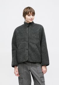 Χνουδωτό σκούρο γκρι μπουφάν με ψηλό γιακά, κούμπωμα με κουμπιά πίεσης, μεγάλες μπροστινές τσέπες και υφή υφάσματος. Κατάλληλο για καθημερινή χρήση.