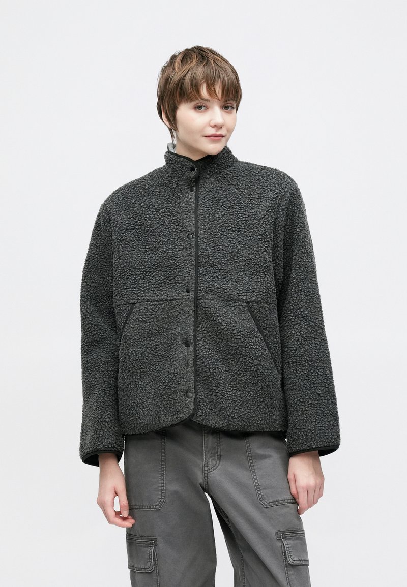 Χνουδωτό σκούρο γκρι μπουφάν με ψηλό γιακά, κούμπωμα με κουμπιά πίεσης, μεγάλες μπροστινές τσέπες και υφή υφάσματος. Κατάλληλο για καθημερινή χρήση.