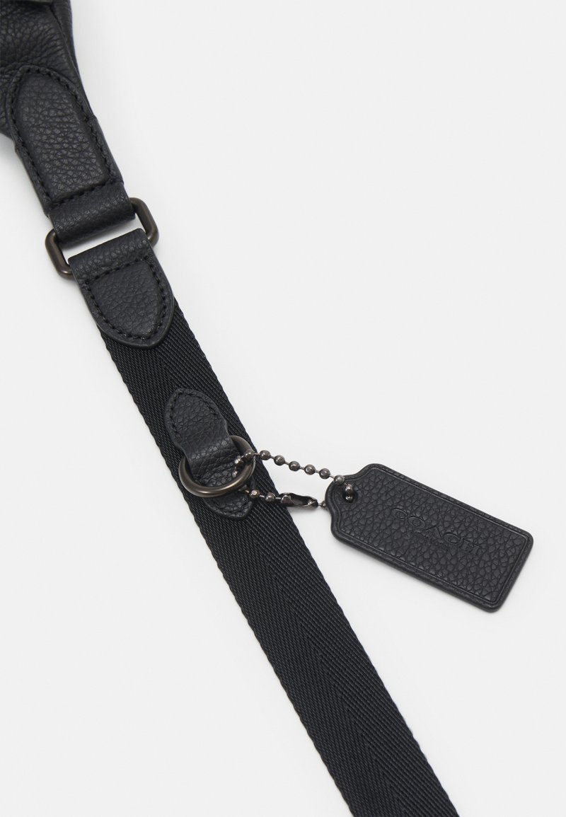 Zwarte verstelbare band met een textuur leer pad, metalen hardware en een afneembare tag die met een balletjesketting is bevestigd.