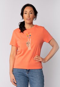 Koraalrode T-shirt met korte mouwen van katoen, met een grafisch ontwerp van een hand met een vredesteken en kleurrijke harten erboven.