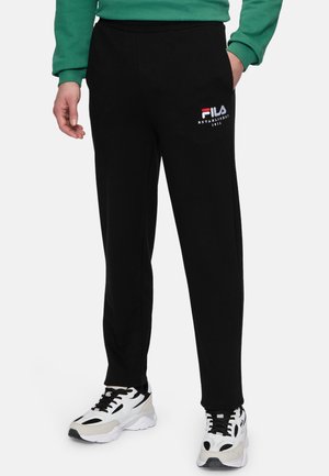 Sorte bomulds joggers med en komfortabel elastisk talje, der har et hvidt og rødt FILA-logo på venstre lår, parret med hvide sneakers.