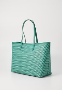 Groene draagtas van textuurmateriaal met een patroon van elkaar overlappende geometrische vormen. Dubbele handvatten in bijpassend groen.