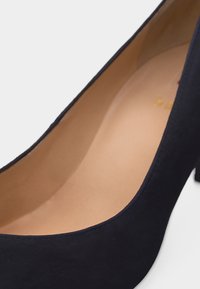 Κοντινό πλάνο μαύρου ψηλοτάκουνου παπουτσιού από σουέντ, εστιάζοντας στην ομαλή ταμπά εσωτερική επένδυση και το καμπυλωτό άνοιγμα.