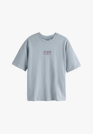 Svjetlosivo kratkih rukava majica s malim pravokutnim ubrusom na prsima koji sadrži japanski i engleski tekst u crnoj i crvenoj boji.