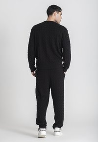 Suéter negro de punto y pantalones a juego con un patrón de trenzado texturizado. Presenta puños y cinturilla de canalé, combinados con zapatillas blancas.