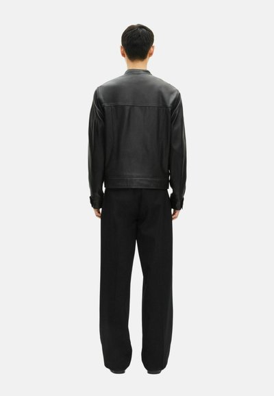 Chaqueta de cuero negro con una textura suave, que presenta un cuello redondo y un corte recto en la parte posterior. Combinada con pantalones negros de corte holgado.