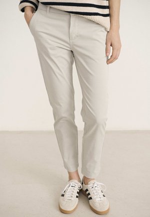 Light beige chino pants with a slim fit and front pockets, paired with white and beige sneakers featuring black stripes.