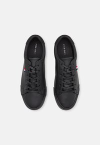 Baskets en cuir noir avec un bout rond, un laçage et des accents subtils rouge, blanc et bleu sur le côté. Texture lisse partout.