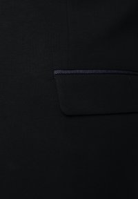 Indumento nero con una texture liscia e una sottile lucentezza, con una piccola tasca applicata evidenziata da un bordo blu scuro.