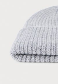 Bonnet en tricot gris avec une texture structurée et un ourlet replié. Fabriqué en laine douce, il présente une apparence légèrement duveteuse.