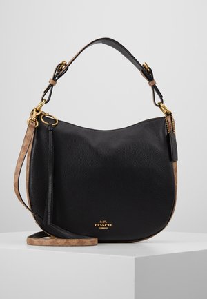 Sac à main Coach en cuir noir avec forme incurvée, ferrures dorées, accents marron, poignée courte et longue bandoulière réglable sur surface blanche.