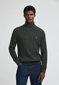 Dunkelgrüner, kabelgestrickter Rollkragensweater, aus weichem Material gefertigt, mit gerippten Bündchen und Saum sowie einem kleinen Logo auf der Brust.