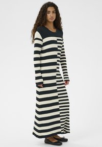 Pikk soonikujuline kleit, millel on mustad ja valged triibud vaheldumisi, ümar kaelus ja küljetukis liikumise mugavuse tagamiseks. Tasased jalanõud.