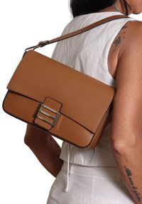 Borsa a spalla in pelle marrone con forma rettangolare, chiusura a pattina e dettaglio con doppia fibbia in argento. Texture liscia con cuciture a contrasto.