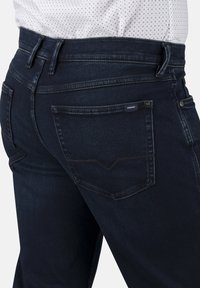 Dunkelblaue Jeans aus Denim mit glatter Textur, die ein klassisches Fünf-Taschen-Design aufweisen und dezente Nähte an den hinteren Taschen haben.