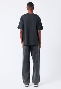 T-shirt nera in cotone oversize con scollatura rotonda, abbinata a jeans grigi a gamba larga caratterizzati da una texture sbiadita e cuciture a contrasto.