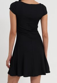 Černé bruslařské šaty s přiléhavým trupem, krátkými rukávy a rozšířenou sukní. Vyrobené z žebrované tkaniny s hladkou strukturou.
