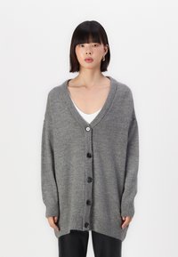 Cárdigan gris de punto con escote en V, botones frontales y dobladillo acanalado. Presenta un ajuste holgado y mangas largas, fabricado en una suave mezcla de lana.