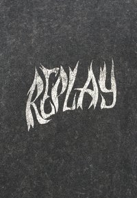 Λευκό υφασμάτινο στιλιζαρισμένο κείμενο "REPLAY" σε σκούρο γκρι φόντο ύφασμα, τα γράμματα φαίνονται επιμηκυμένα και ελαφρώς παραμορφωμένα.