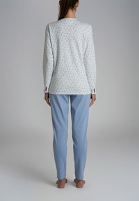 Top a maniche lunghe bianco con stampa floreale blu, abbinato a pantaloni da pigiama azzurri. Entrambi gli articoli presentano una vestibilità rilassata e una morbida trama.