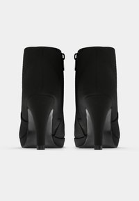 Botas negras de tobillo con un acabado texturizado, tacones de aguja altos y cremalleras traseras. Presentan una punta suave y un diseño estilizado.