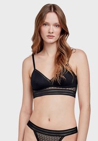 Bralette en dentelle noire avec des bordures en dentelle transparente, des bretelles ajustables et un motif floral. Accompagné de culottes en dentelle noire assorties avec des accents de bande.