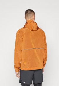 Heren oranje lichte jacket met een capuchon, textuurstof, reflecterende strip over de achterkant en elastische manchetten.