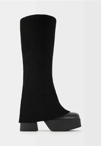 Botte noire montante en tricot côtelé avec talon plateforme épais et bout arrondi, vue de côté sur fond clair uni.