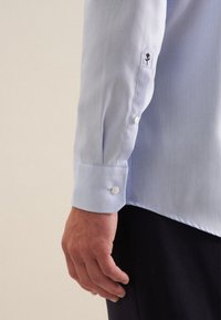 Camicia azzurro chiaro con una texture liscia, polsini abbottonati e un design floreale ricamato sulla manica.