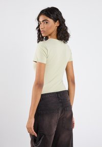 Top ajustado de manga corta en verde claro, combinado con pantalones cargo sueltos de color negro y textura, que presentan grandes bolsillos traseros y una silueta relajada.
