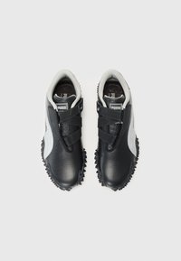 Paire de chaussures de sport Puma noire et blanche avec semelles texturées et sangles croisées sur un fond uni clair.