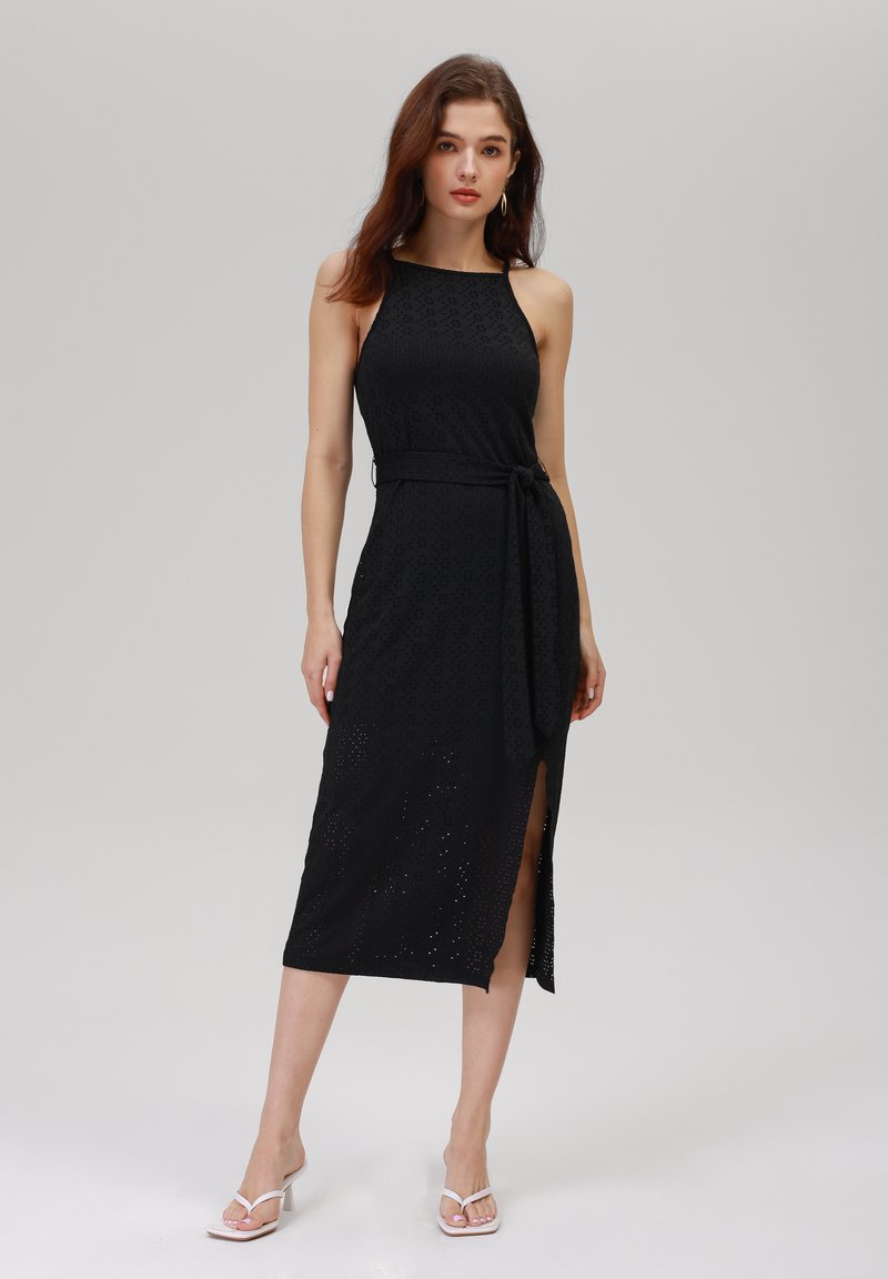 Rochie neagră cu guler halter, cu modele florale din ochiuri, talie cu curea și crăpătură pe lateral. Asortată cu sandale albe cu toc.