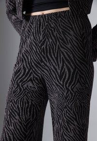 Zwarte stoffen broek met een zebra-streep patroon in zilver glitter, met een ontspannen pasvorm en subtiele textuur.