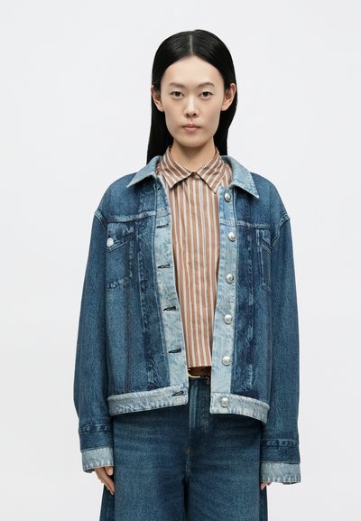 Casaco de ganga com detalhes em azul claro e botões prateados, com um corte descontraído, dois bolsos frontais, combinado com uma camisa às riscas castanha.