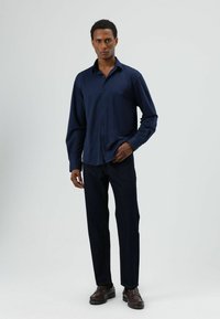 Marineblauw overhemd met lange mouwen en knopen, met een losse pasvorm, gecombineerd met donkere jeans en bruine schoenen. Gladde stof, subtiele glans en klassieke kraag.