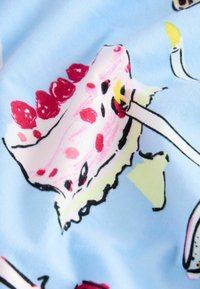Blått tyg med färgglada illustrationer av tårtstycken med körsbär på toppen och tända födelsedagsljus.