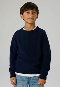 Marineblauer Strickpullover mit rundem Ausschnitt und langen Ärmeln, über einem weißen T-Shirt getragen, kombiniert mit hellblauen Denim-Jeans.