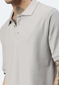 Polo shirt grigio chiaro realizzato in tessuto testurizzato, con colletto e patta con due bottoni. Maniche corte con una vestibilità rilassata.