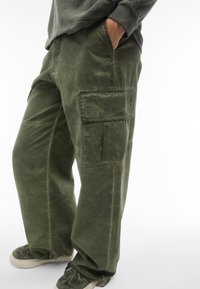 Pantaloni cargo verdi in tessuto morbido, con una vestibilità comoda, tasche laterali e un sottile motivo cucito sul tessuto.