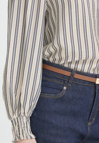 Blouse à boutons rayée beige et marine, avec poignets élastiques. Associée à un jean bleu fonc é et une ceinture en cuir marron.