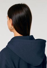 Felpa blu navy con un ampio cappuccio morbido, caratterizzata da una texture a coste e cuciture in vista. Orecchini a cerchio dorati completano il design.