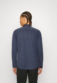 Dark blue long-sleeve shirt with a collared neck, subtle texture, and button details on the cuffs, shown from the back.